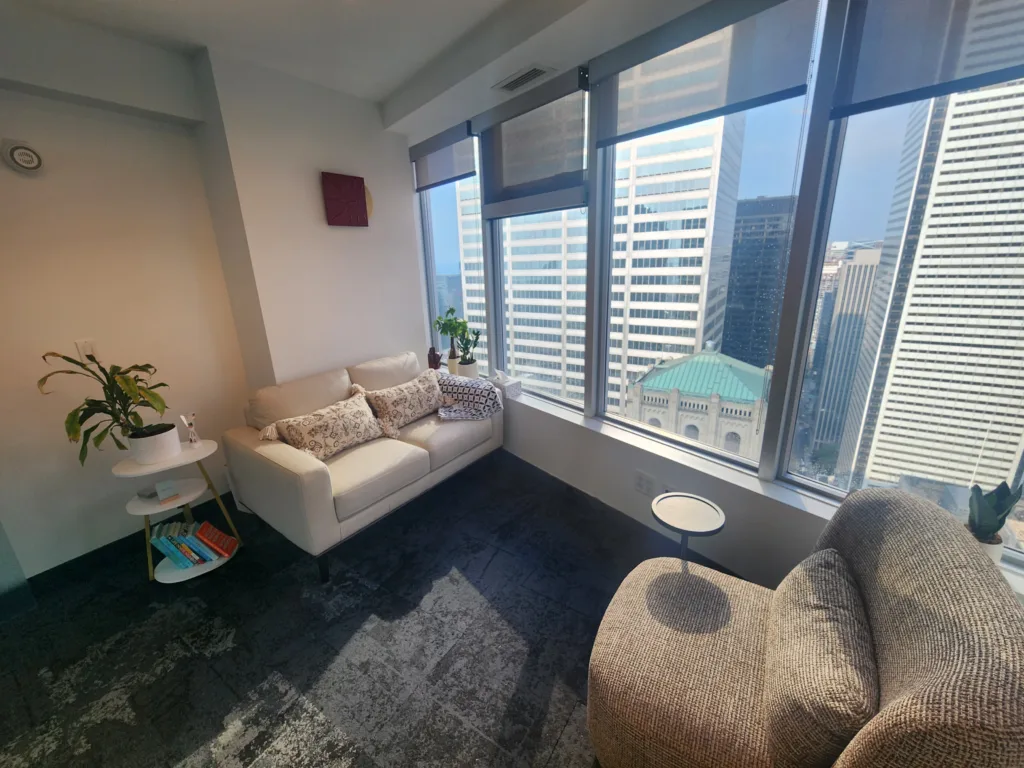 Therapy room with a cream sofa and floor-to-ceiling windows overlooking downtown Toronto